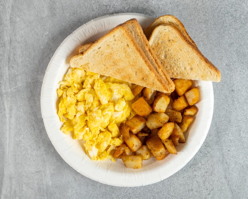 A breakfast plate with scrambled eggs, crispy home fries, and two slices of toast.