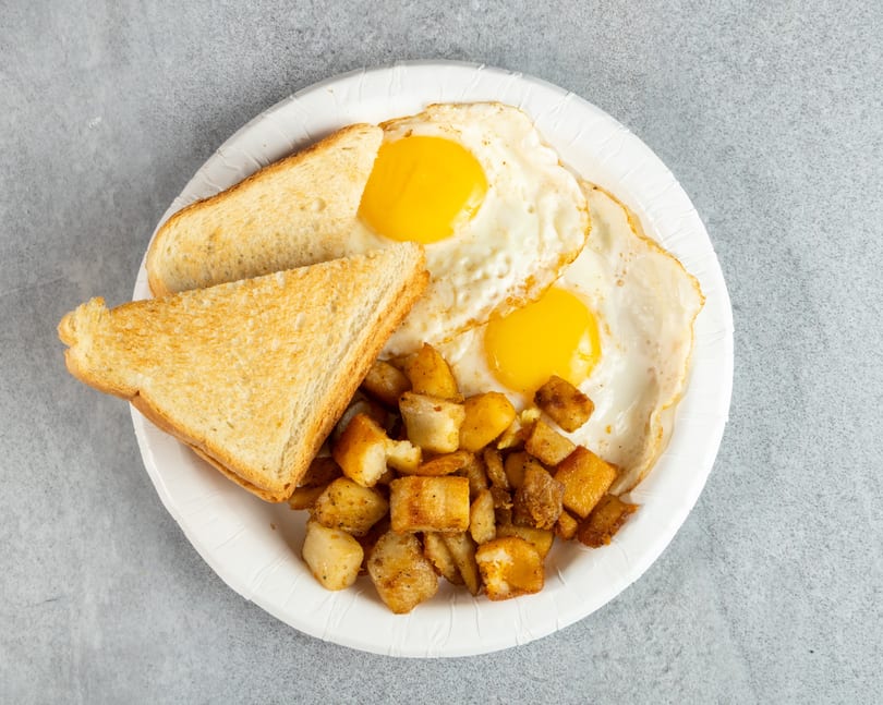 Breakfast plate with two fried eggs, golden-brown home fries, and two slices of toast.
