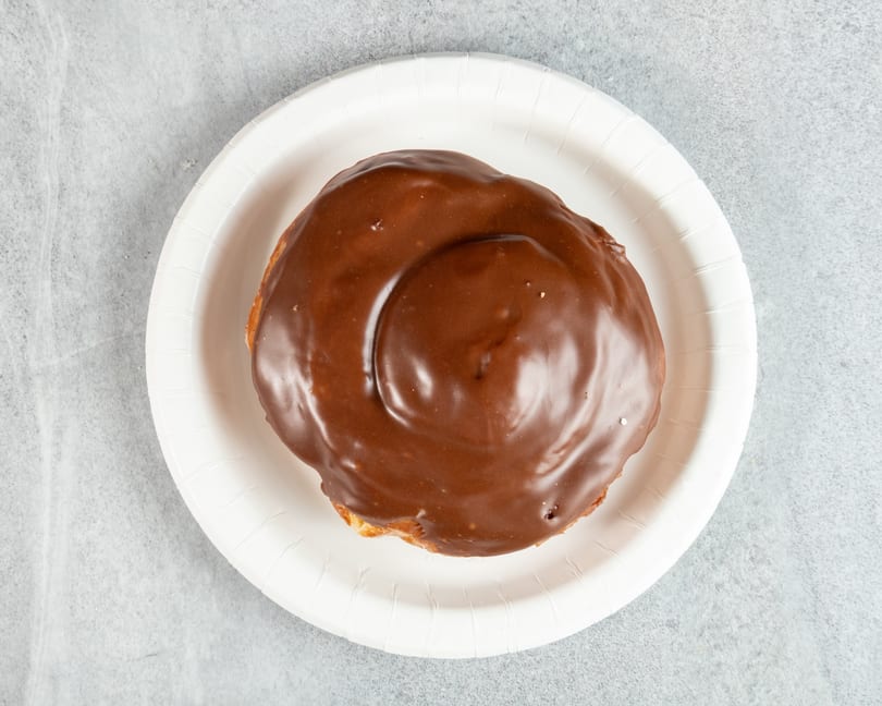 Overhead view of a chocolate-glazed pastry on a white paper plate.