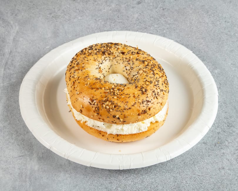 Everything bagel with cream cheese on a white paper plate.