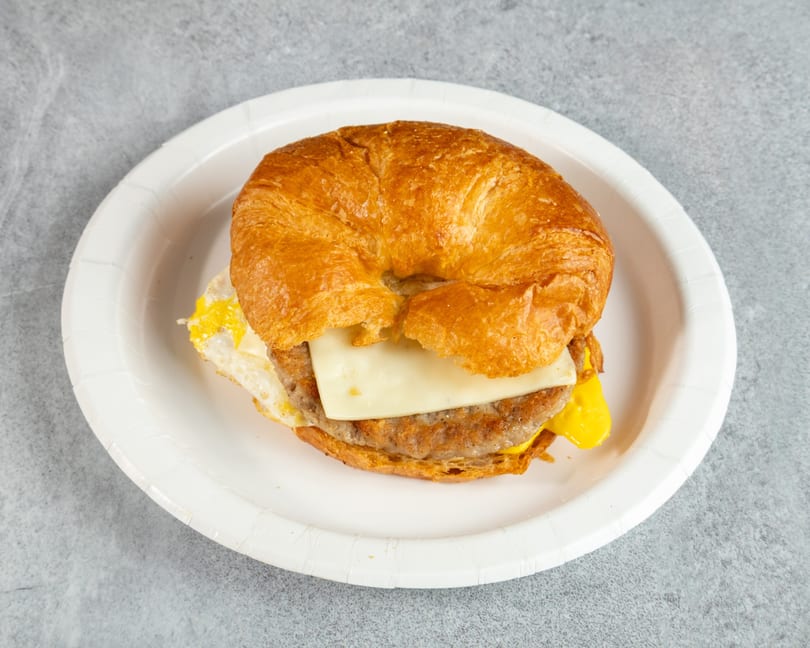 Croissant breakfast sandwich with sausage, egg, and cheese on a white paper plate.