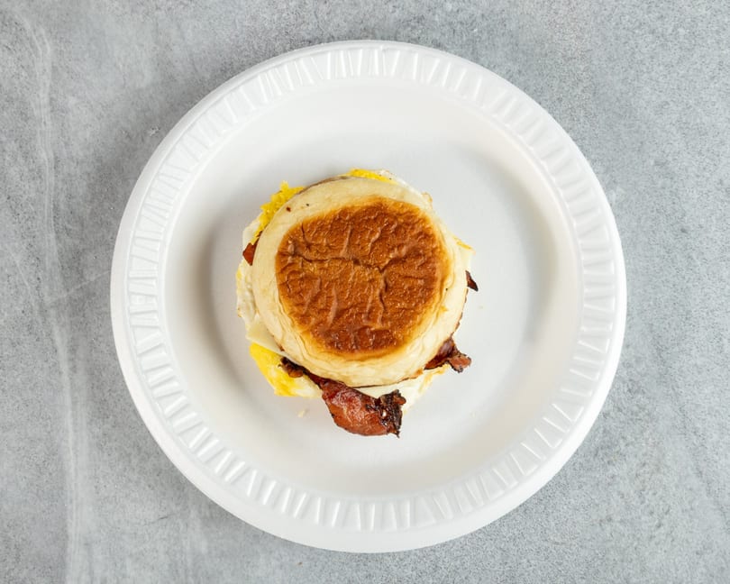 Breakfast sandwich with bacon, egg, and cheese on a toasted bun, served on a white plate.